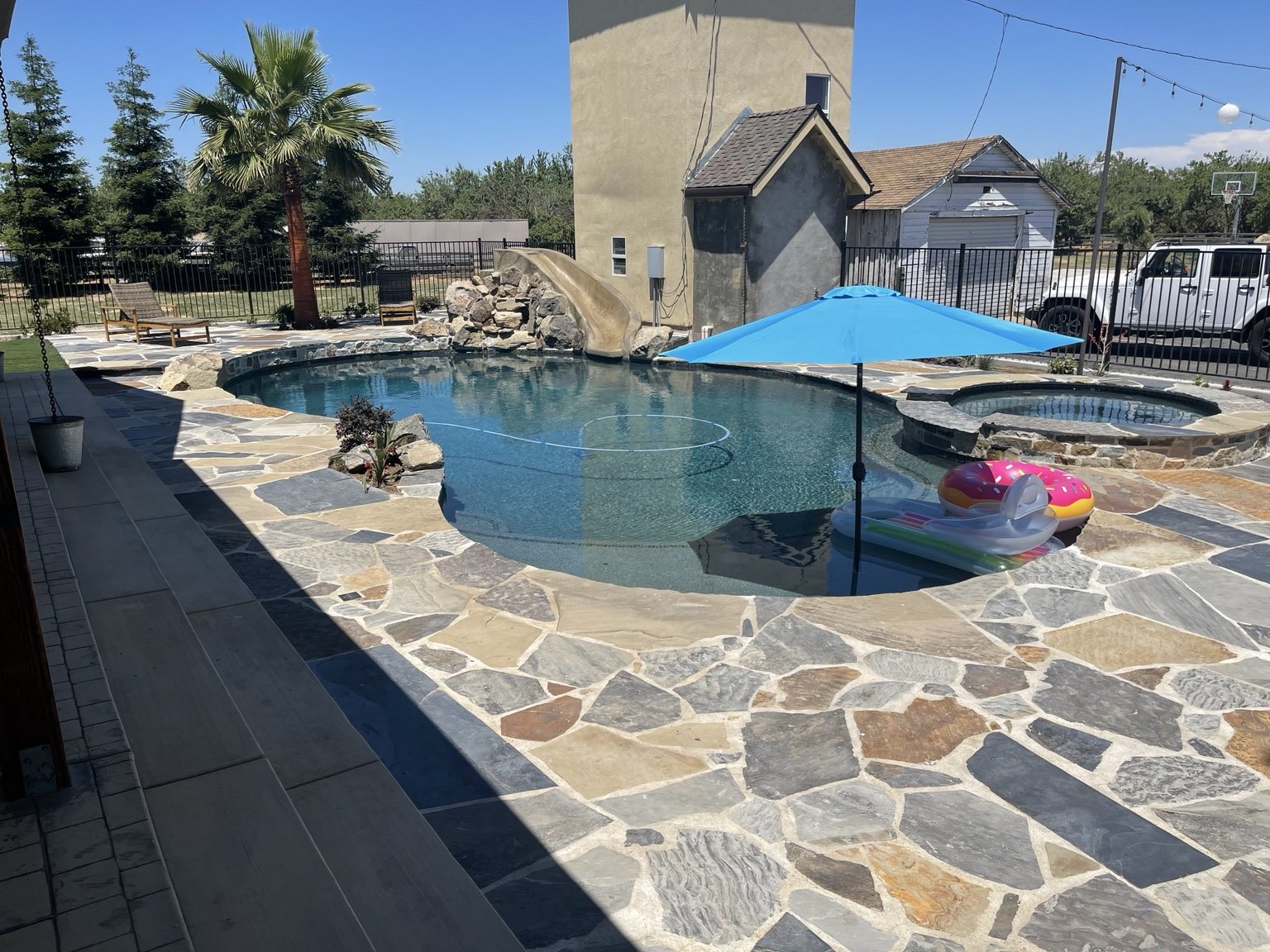 Custom swimming pool with spa, waterslide, and natural stone patio